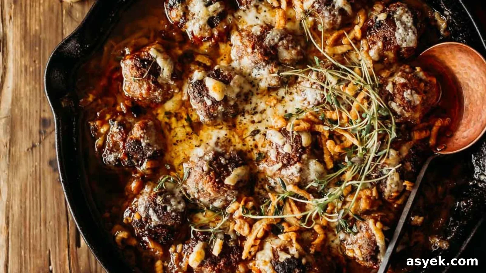 French onion meatballs covered in melted cheese and caramelized onions in a deep skillet.