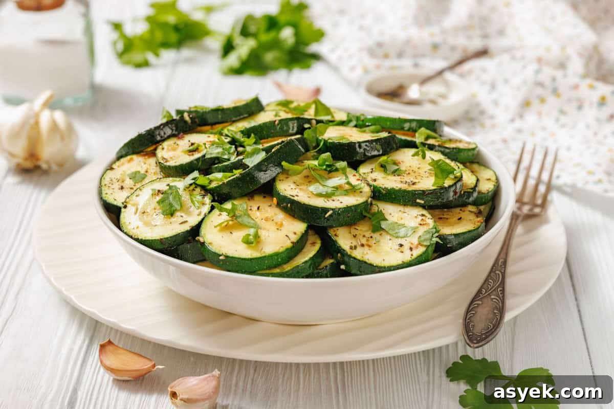 A white bowl filled with sliced Sautéed Zucchini with Garlic and Herbs, garnished with chopped herbs, is placed on a white plate with a fork nearby.