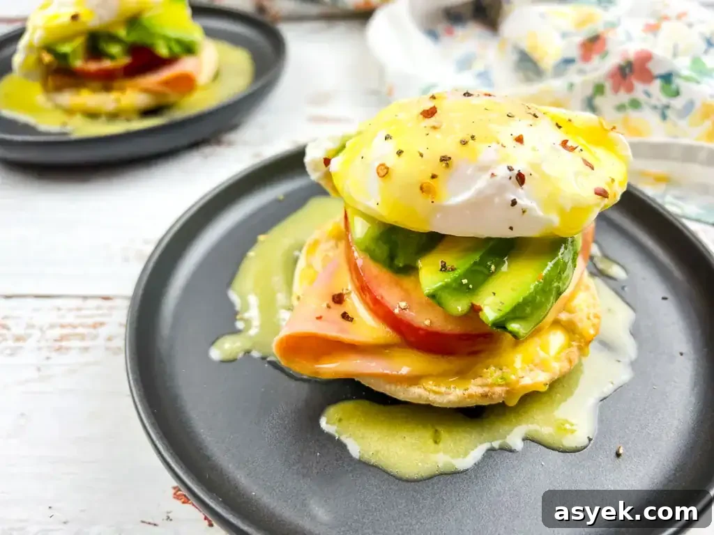 Eggs benedict with ham and avocado on an English muffin served on a black plate.