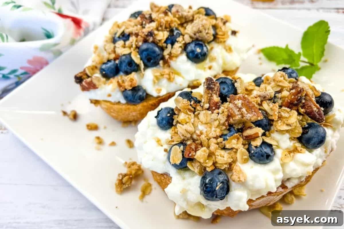 A plate of cottage cheese toast with blueberries, next to a honey dipper.