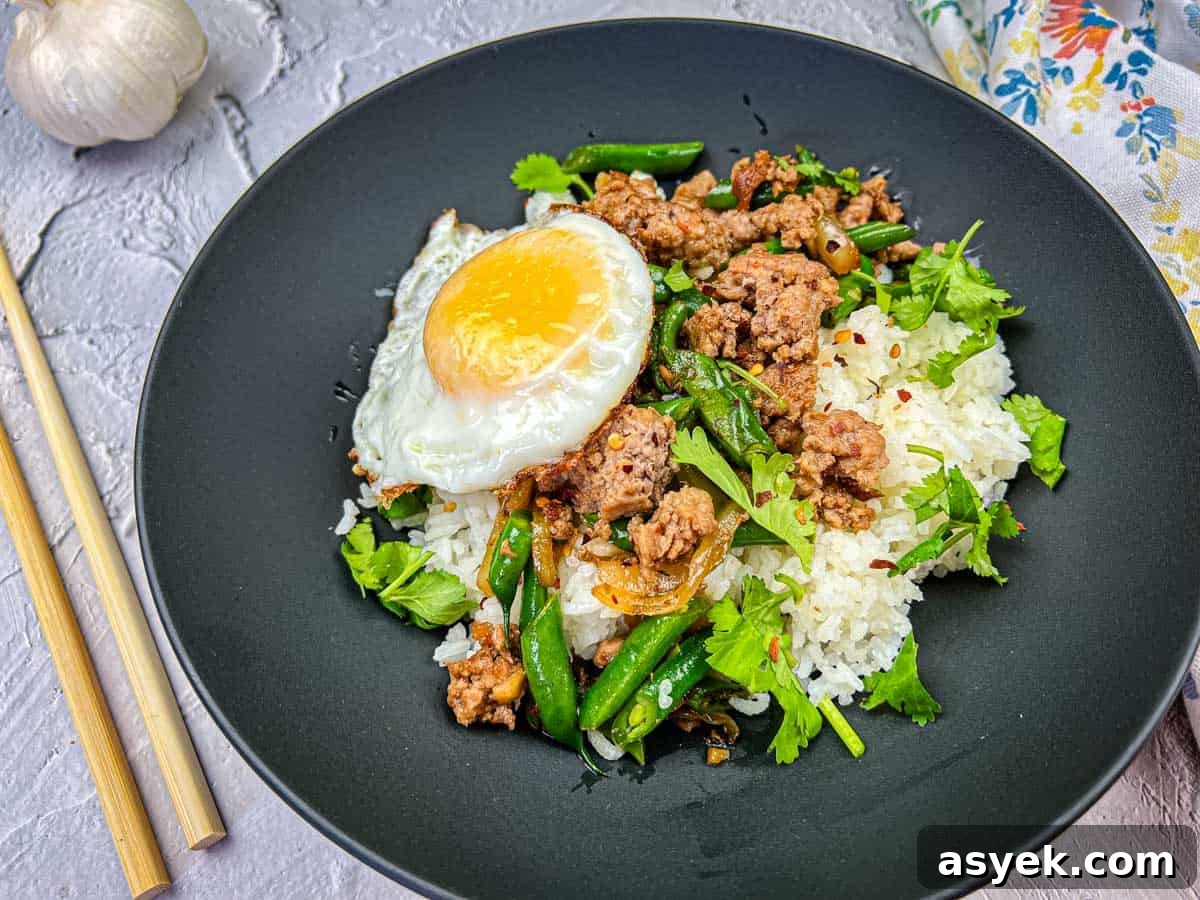 A plate of Thai pork & Green beans with rice, topped with a fried egg, served with chopsticks on the side.