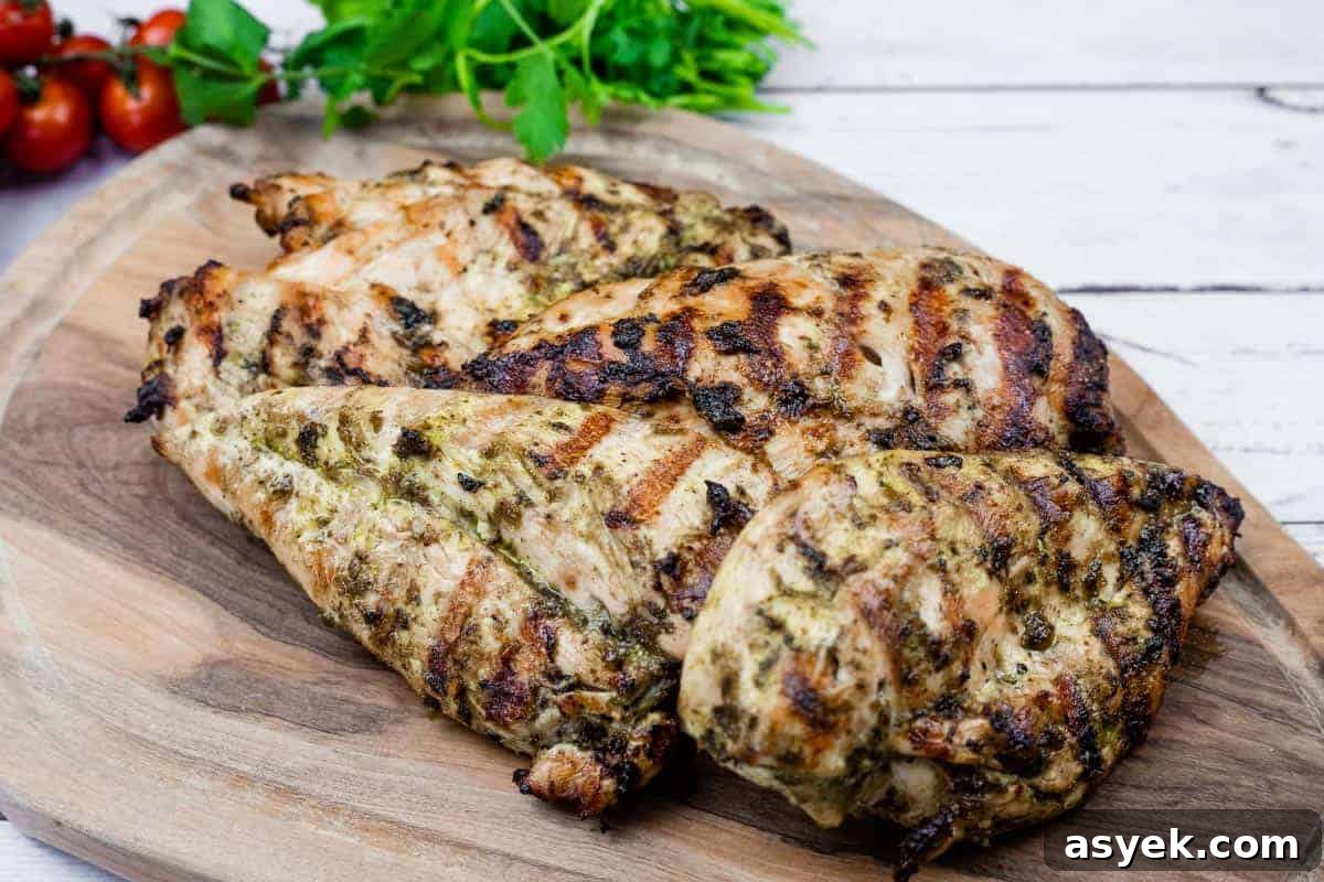 Grilled chicken on a wooden board with cilantro and tomatoes in the back.