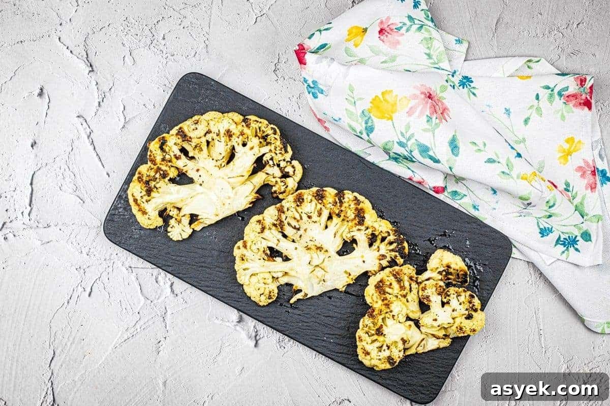 Three pieces of grilled cauliflower steaks on a black plate.