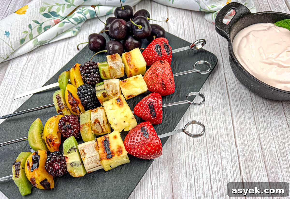 Four pieces of grilled fruit skewers on a slate plate with a bowl of cherry dip.