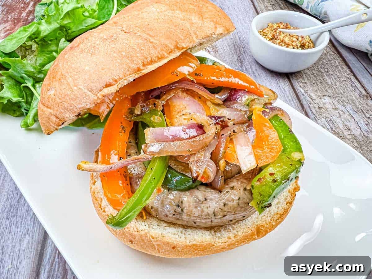 A sandwich with grilled sausage & peppers, and onions on a plate.