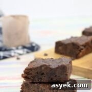 25+ Dairy-Free, Gluten-Free Protein Desserts 12 Two chocolate brownies stacked with more brownies on a cutting board and a scoop of protein powder on a blue linen