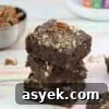 25+ Dairy-Free, Gluten-Free Protein Desserts 15 Three chocolate protein brownies stacked with protein powder behind them.