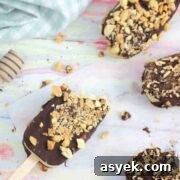 25+ Dairy-Free, Gluten-Free Protein Desserts 30 Chocolate coated ice cream bars with peanuts on parchment paper with one having a bite out of it.
