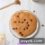 25+ Dairy-Free, Gluten-Free Protein Desserts 40 White plate with large single serving protein cookie with chocolate chips in it and a stick of honey behind it.