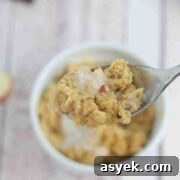 25+ Dairy-Free, Gluten-Free Protein Desserts 41 Apple mug cake in a white ramekin with coconut milk on top and a spoon pulling out of it.