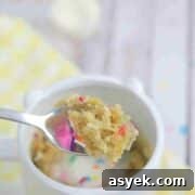 25+ Dairy-Free, Gluten-Free Protein Desserts 42 Spoon pulling out of a mug with protein mug cake with sprinkles on it and the mug on a yellow linen.