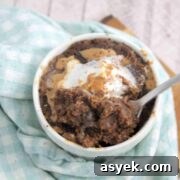25+ Dairy-Free, Gluten-Free Protein Desserts 43 Chocolate protein powder mug cake topped with peanut butter and coconut whipped cream in a white mug on a blue linen.