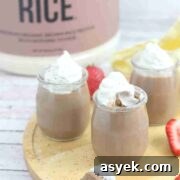 25+ Dairy-Free, Gluten-Free Protein Desserts 6 Three glass jars of chocolate protein mousse topped with coconut whipped cream on a wooden cutting board with strawberries around them and a spoonful in front.