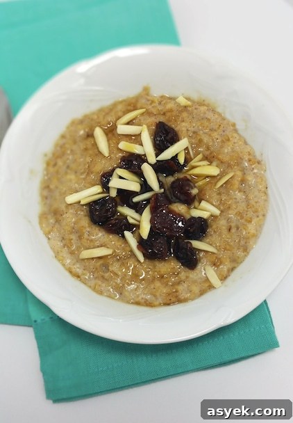 A close up of a bowl of cooked steel-cut oats, with dried cherries, cut almonds.