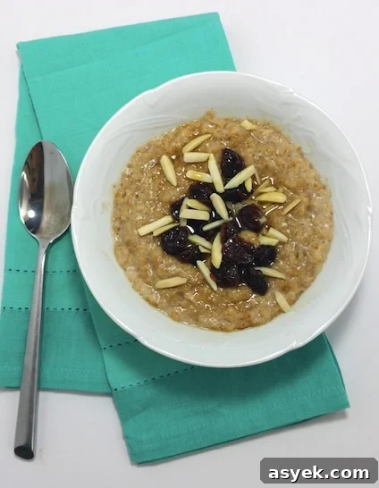 A bowl of cooked steel-cut oats, with dried cherries, cut almonds on a green napkin next to a spoon.