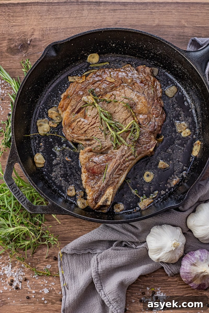 ribeye in a cast iron pan with thyme, rosemary and sliced garlic
