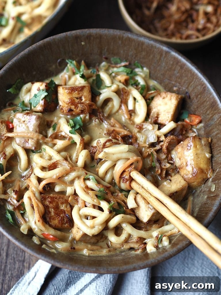 15-Minute Curry Udon Recipe with Tofu and Crispy Shallots 3 A bowl of curry udon soup being stirred withy chopsticks.