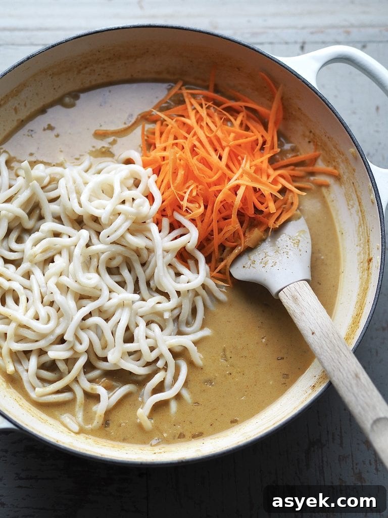 15-Minute Curry Udon Recipe with Tofu and Crispy Shallots 8 Shredded carrot and udon noodles being stirred into a creamy curry soup.