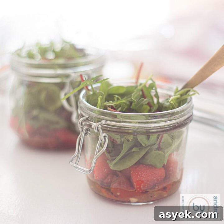 Two jars filled with fresh salad with lettuce, strawberries and honey mustard dressing